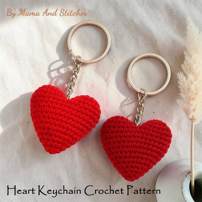 Peut inclure: Deux porte-cl&eacute;s en forme de c&oelig;ur rouge crochet&eacute;s, avec des cha&icirc;nes et des anneaux argent&eacute;s. Les porte-cl&eacute;s sont faits &agrave; la main et pr&eacute;sentent un aspect textur&eacute; et tricot&eacute;. Le texte "Heart Keychain Crochet Pattern" est visible.