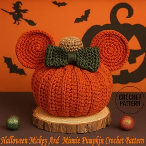 Può includere: Una zucca all'uncinetto arancione con orecchie circolari, un fiocco verde e una parte superiore beige. La zucca è appoggiata su una fetta di legno, con una pallina verde glitterata e una pallina rossa glitterata nelle vicinanze. Il testo "Halloween Mickey And Minnie Pumpkin Crochet Pattern" è in basso.