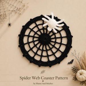 May include: A black crocheted spider web coaster with a small white crocheted spider attached to the top. The text Spider Web Coaster Pattern by Mama And Stitches is printed at the bottom of the image, which also features dried foliage.