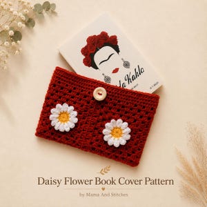 Peut inclure: Une housse de livre crochetée rouge foncé ornée de deux appliqués marguerites blancs et jaunes et d'un bouton en bois clair. La housse est posée sur un livre illustré de Frida Kahlo avec le texte Daisy Flower Book Cover Pattern inscrit dessus.