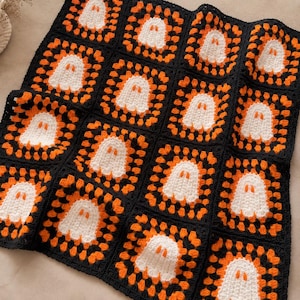 May include: A handmade crochet blanket composed of square motifs, each featuring a white ghost centered against a vibrant orange and black background. The repeating pattern consists of sixteen individual squares joined together in a grid formation.