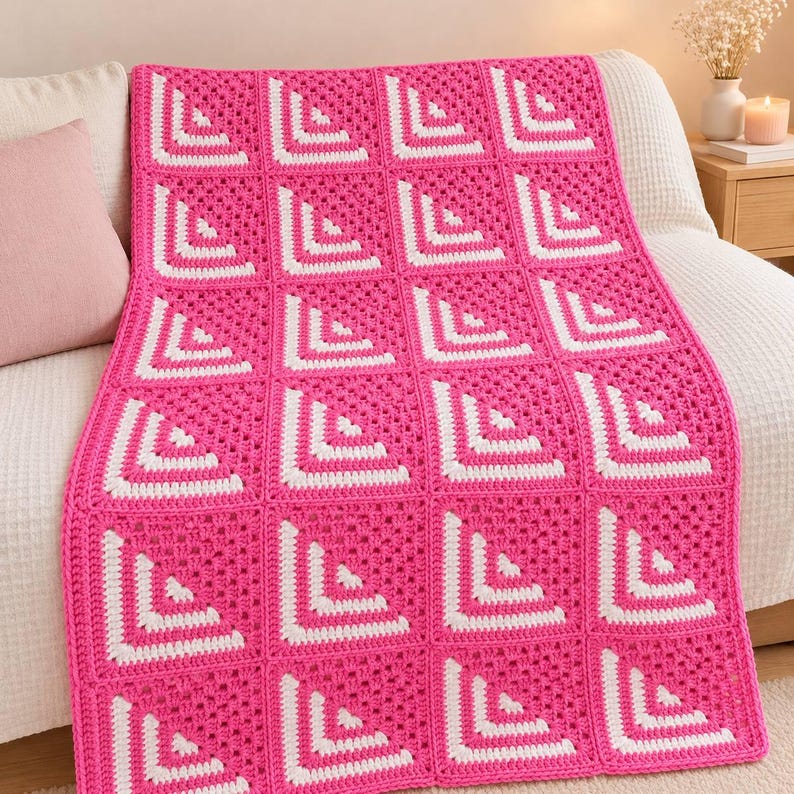 May include: A rectangular crochet blanket featuring a repeating pattern of square motifs. Each square is composed of alternating rows of vibrant hot pink and crisp white yarn, arranged to create a geometric corner design across the entire piece.