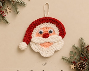 May include: A crocheted Santa Claus ornament featuring a red hat with a white pom-pom, a peach-colored face, a white mustache and beard, and two plastic googly eyes. The text "Santa Claus Ornament Pattern by Mama And Stitches" is visible.