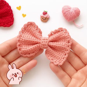 Pu&ograve; includere: Un fiocco all'uncinetto color pesca con un bordo testurizzato e smerlato. Il fiocco &egrave; accompagnato da un piccolo ciondolo a forma di cupcake sorridente, un gomitolo di lana rosa a forma di cuore, un pezzo all'uncinetto rosso e due cuori.