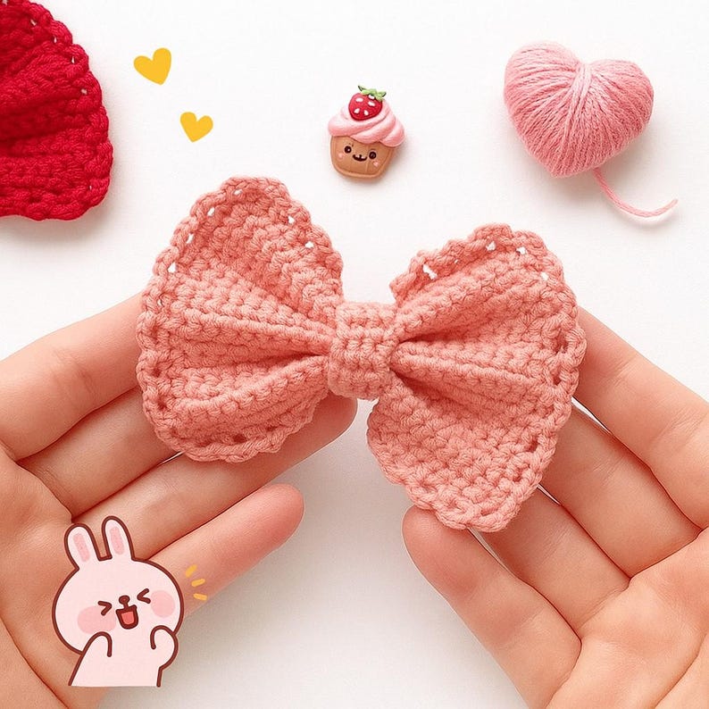 Pu&ograve; includere: Un fiocco all'uncinetto color pesca con un bordo testurizzato e smerlato. Il fiocco &egrave; accompagnato da un piccolo ciondolo a forma di cupcake sorridente, un gomitolo di lana rosa a forma di cuore, un pezzo all'uncinetto rosso e due cuori.