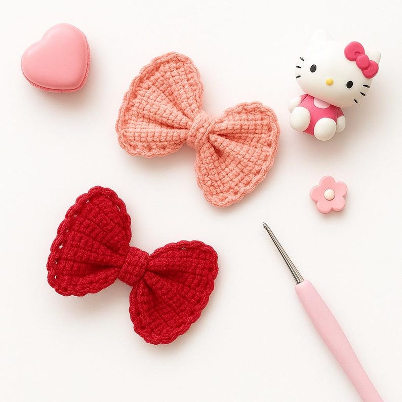Pu&ograve; includere: Due fiocchi all'uncinetto, uno rosa chiaro e uno rosso scuro, sono disposti insieme a un macaron rosa a forma di cuore, una piccola statuetta di Hello Kitty, un minuscolo ciondolo a forma di fiore rosa e un uncinetto rosa chiaro su sfondo bianco.