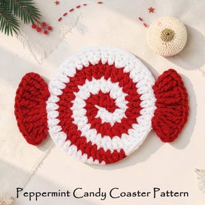 May include: A handmade crochet coaster in the shape of a peppermint candy. The coaster features a spiral design with alternating red and white stripes, with red candy wrapper ends. A smaller, round, cream-colored coaster is also visible.