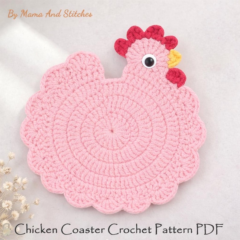 Pode incluir: Um porta-copos de croch&ecirc; em forma de galinha rosa claro com crista vermelha, bico amarelo e um olho de pl&aacute;stico preto e branco. O texto By Mama And Stitches e Chicken Coaster Crochet Pattern PDF &eacute; vis&iacute;vel na imagem.
