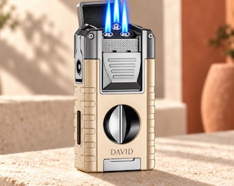 Peut inclure: Un briquet en métal de couleur or et gris acier avec trois flammes bleu vif émanant du sommet. L'appareil rectangulaire possède un coupe-cigare circulaire intégré sur la face avant avec le mot DAVID imprimé en noir en dessous.
