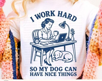 May include: White t-shirt with a blue graphic of a woman working at a desk with a dog. The text reads "I WORK HARD SO MY DOG CAN HAVE NICE THINGS." The design includes a laptop, lamp, and alarm clock.