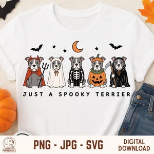 Puede incluir: Una camiseta blanca con un gráfico de cinco perros terrier grises disfrazados de Halloween, incluyendo un diablo, un fantasma, un esqueleto, una calabaza y la parca. El texto "JUST A SPOOKY TERRIER" está impreso bajo los perros con murciélagos.
