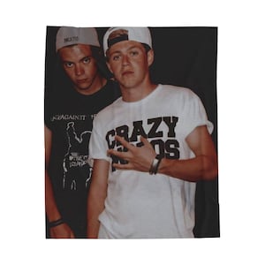 May include: A white t-shirt with the words "CRAZY KIDS" in black block letters. The image also shows a person wearing a white cap and a black bracelet. Another person is wearing a black t-shirt and a gray cap.