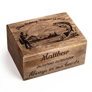 May include: Wooden box with engraved fishing scene and text. The box features a fisherman, a leaping fish, and the words "Gone Fishing, Forever at Rest." It also includes the name "Matthew" and dates, with the phrase "Always in our hearts."