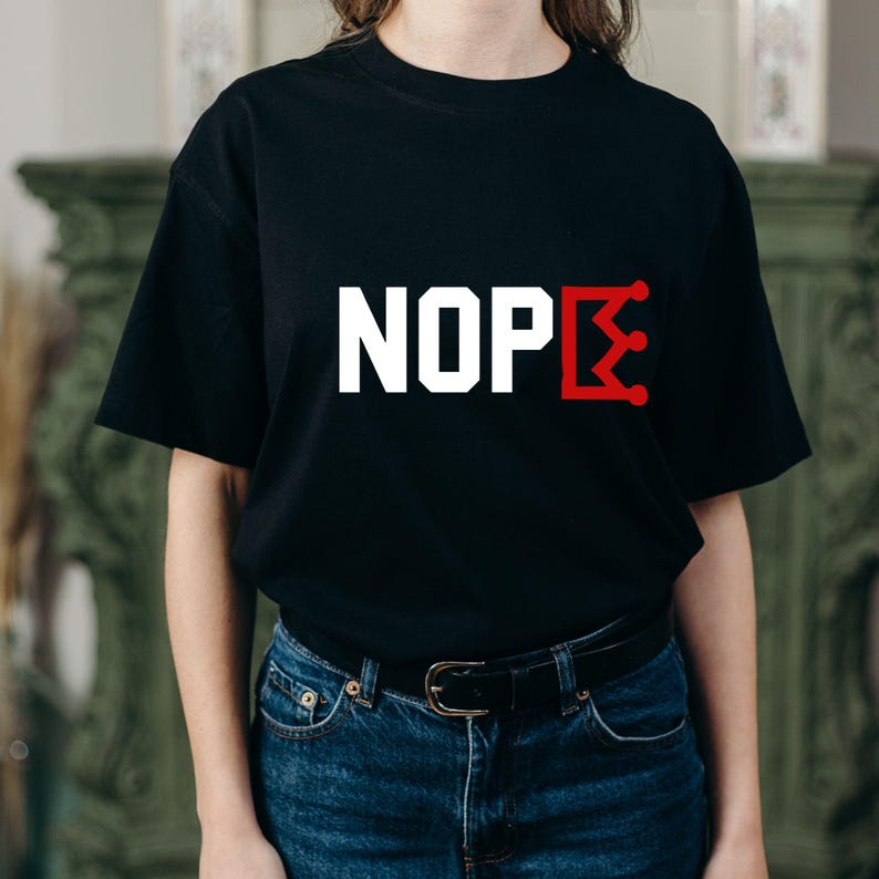 K&ouml;nnte beinhalten: Schwarzes T-Shirt mit dem Wort "NOPE" in Wei&szlig;, wobei das "E" durch ein rotes Kronen-Design ersetzt wird. Das T-Shirt wird mit einer blauen Jeans getragen. Das Bild zeigt eine Person, die das T-Shirt tr&auml;gt.