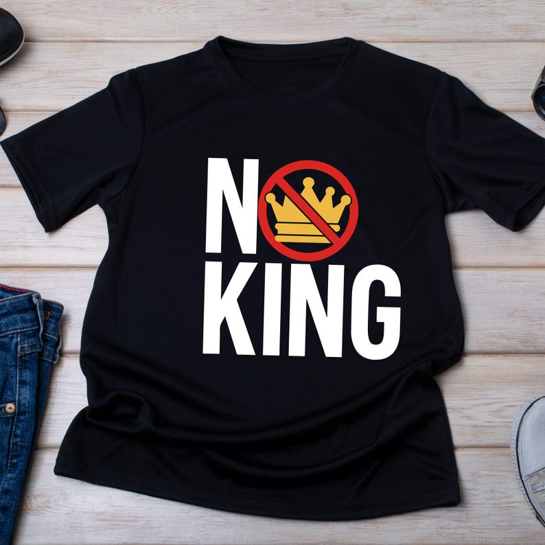 K&ouml;nnte beinhalten: Schwarzes T-Shirt mit den Worten "NO KING" in gro&szlig;en wei&szlig;en Blockbuchstaben. Der Buchstabe "O" zeigt eine goldene Krone, die mit einem roten Kreis und einer roten Diagonale durchgestrichen ist. Das Shirt ist aus weichem Material.