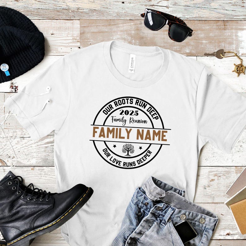May include: White t-shirt with a circular design that reads "OUR ROOTS RUN DEEP 2025 Family Reunion FAMILY NAME OUR LOVE RUNS DEEPER". The shirt is on a light wood grain surface with black boots, sunglasses, and jeans.