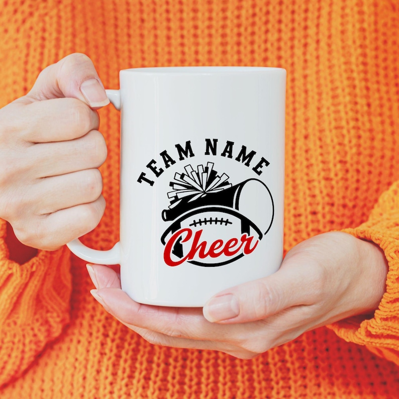 May include: White ceramic mug with a black and red cheerleading design. The design includes a megaphone, pom-poms, and a football, with the word "Cheer" in red script. The mug also has the words "Team Name" in a black, bold font.
