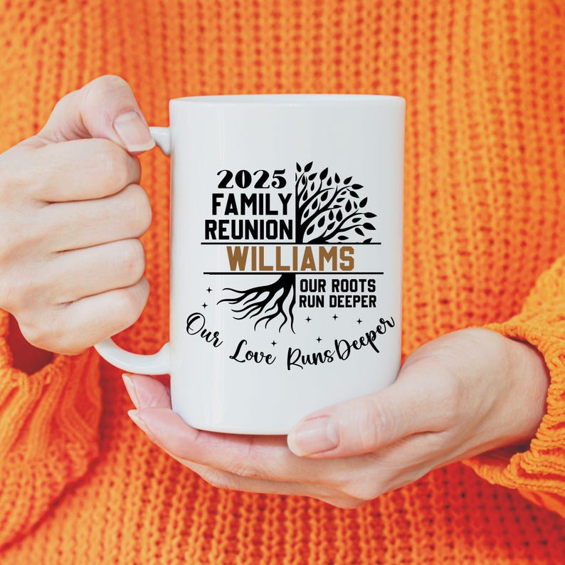 May include: White ceramic mug with black text that reads "2025 Family Reunion Williams Our Roots Run Deeper Our Love Runs Deeper" and a tree graphic. The mug is held by a person wearing an orange sweater.