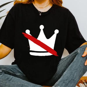 K&ouml;nnte beinhalten: Schwarzes T-Shirt mit einem wei&szlig;en Kronen-Design, das mit einem roten Strich durchgestrichen ist. Die Grafik befindet sich auf der Vorderseite des Shirts. Das Oberteil hat kurze &Auml;rmel und einen Rundhalsausschnitt.