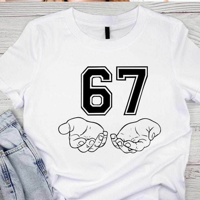 K&ouml;nnte beinhalten: Wei&szlig;es T-Shirt mit der Zahl "67" in schwarzer, college-artiger Schrift. Unter den Zahlen befinden sich zwei offene H&auml;nde, ebenfalls in Schwarz. Das Design ist mittig auf dem Shirt platziert.