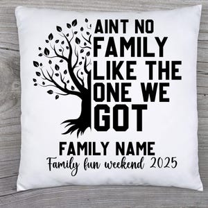 May include: White square pillow with a black tree graphic and the text "AINT NO FAMILY LIKE THE ONE WE GOT." Below the text is "FAMILY NAME" and "Family fun weekend 2025" in a script font.