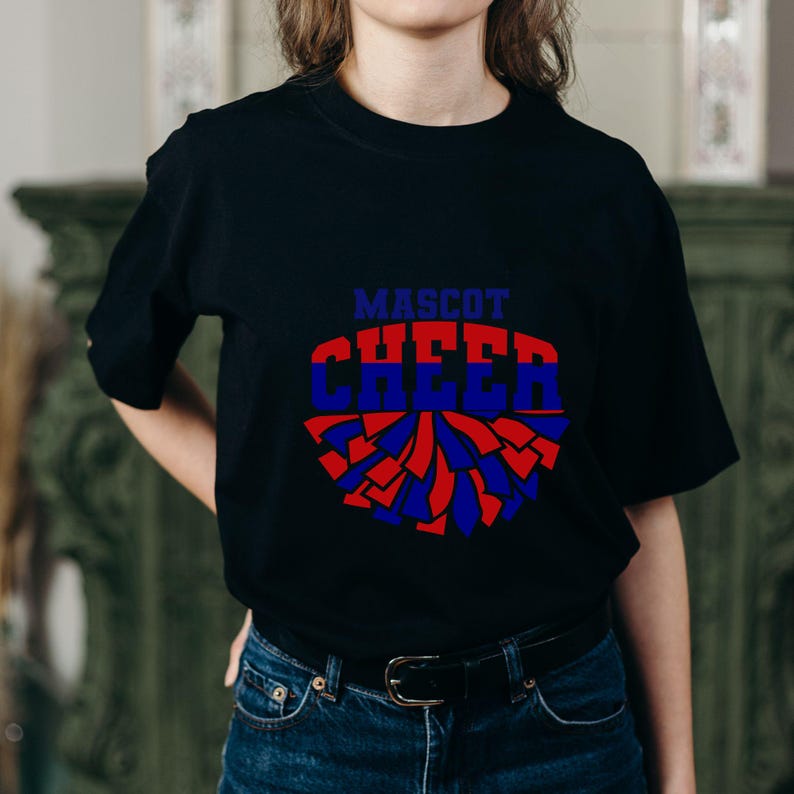 May include: Black t-shirt with a blue and red pom-pom design. The shirt features the words "MASCOT CHEER" in blue and red block letters. The design is centered on the front of the shirt.