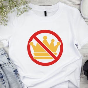 K&ouml;nnte beinhalten: Wei&szlig;es T-Shirt mit einem gelben Kronen-Design in einem roten Kreis, durchgestrichen mit einer roten Linie. Die Grafik ist zentriert. Das Shirt besteht aus einem weichen Material.