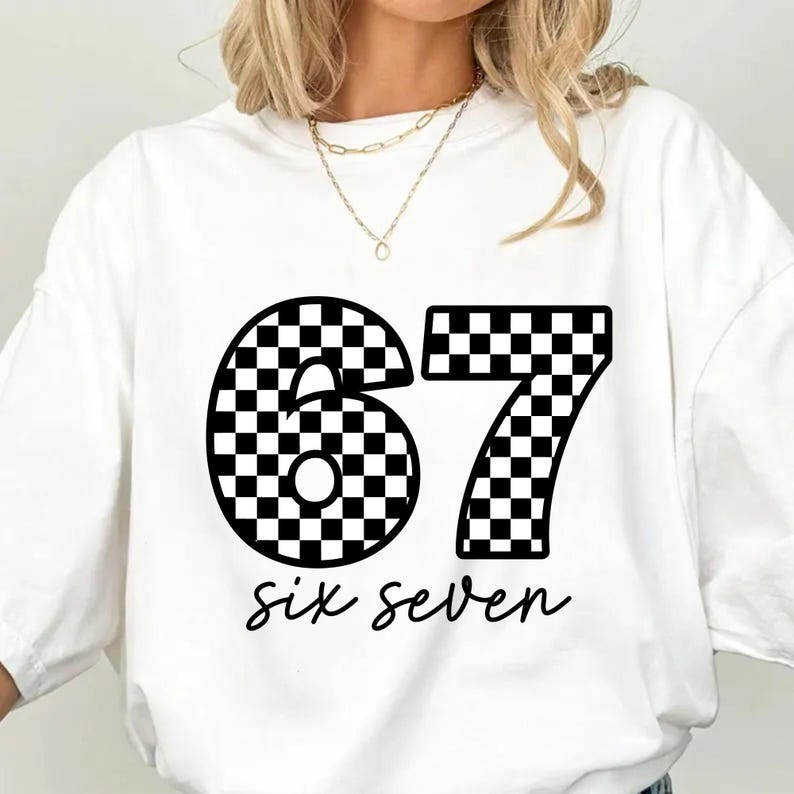 K&ouml;nnte beinhalten: Wei&szlig;es T-Shirt mit einer gro&szlig;en schwarz-wei&szlig; karierten Zahl 67. Unter den Zahlen stehen die Worte "six seven" in Schreibschrift. Das T-Shirt hat einen l&auml;ssigen Stil.