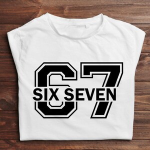 K&ouml;nnte beinhalten: Wei&szlig;es T-Shirt mit der Zahl "67" in fetter, schwarzer Schrift im College-Stil. Darunter stehen die Worte "SIX SEVEN" in einer passenden Schriftart.