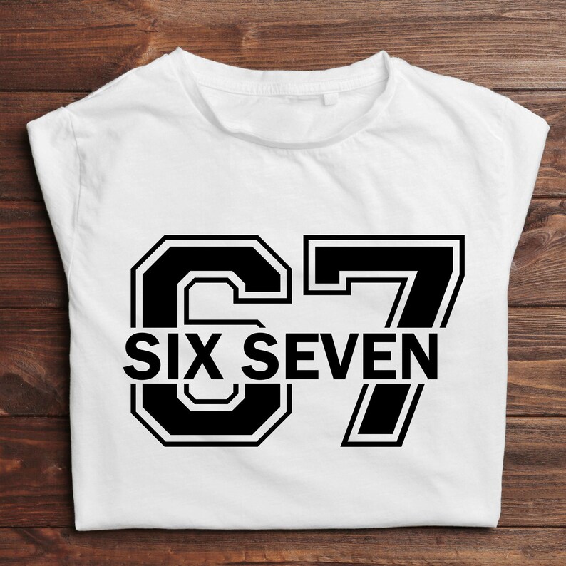 K&ouml;nnte beinhalten: Wei&szlig;es T-Shirt mit der Zahl "67" in fetter, schwarzer Schrift im College-Stil. Darunter stehen die Worte "SIX SEVEN" in einer passenden Schriftart.