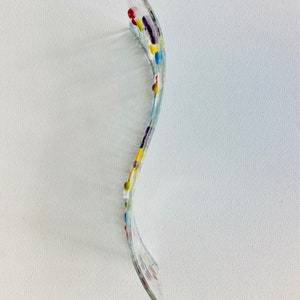 May include: A clear glass piece with a wavy shape and colorful dots in shades of red, yellow, blue, and purple.