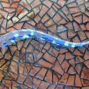 May include: A blue and white glass mosaic tile with a clear, wavy glass piece on top. The mosaic tile is made of small, irregular pieces of glass.