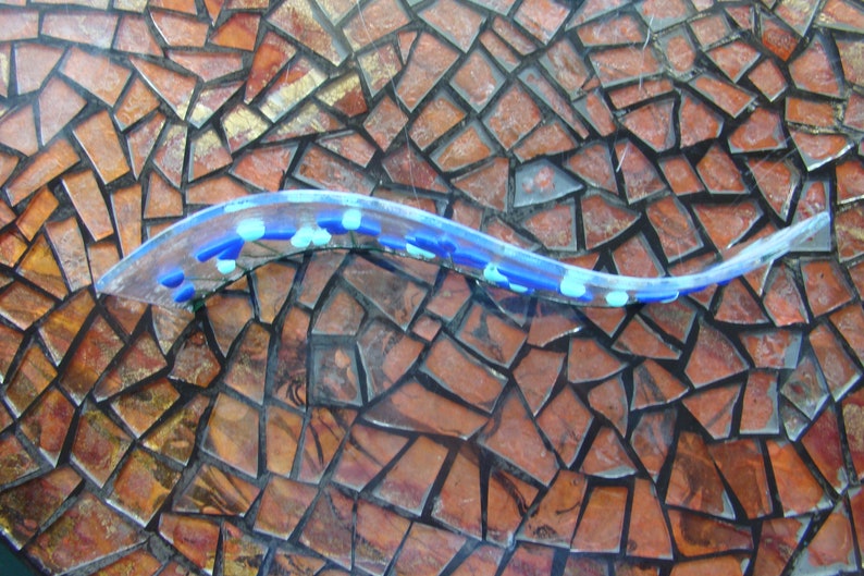 May include: A blue and white glass mosaic tile with a clear, wavy glass piece on top. The mosaic tile is made of small, irregular pieces of glass.