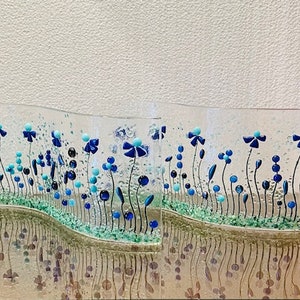 May include: Two glass panels with a wavy design featuring blue and turquoise flowers and green leaves. The panels are set against a white background.