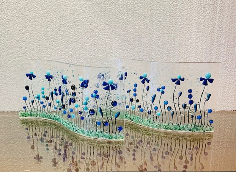 May include: Two glass panels with a wavy design featuring blue and turquoise flowers and green leaves. The panels are set against a white background.