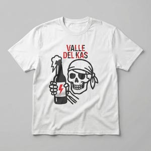 Può includere: T-shirt bianco con un design grafico raffigurante un teschio con una bandana e una bottiglia con un fulmine. Il testo "VALLE DEL KAS" è stampato in rosso sopra il teschio.