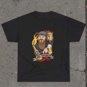 May include: Black t-shirt with a cartoon illustration of a bearded man holding a beer and a bottle with flames. The text "¡NO PASARAN!" is on a banner below the image. The man is wearing a hat and has a raised fist.