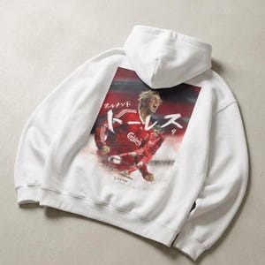 Puede incluir: Sudadera con capucha blanca con un gráfico de un jugador de fútbol con uniforme rojo. El gráfico incluye texto japonés y un fondo rojo y blanco. La sudadera tiene capucha y mangas largas.