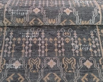 Puede incluir: Una alfombra de color gris oscuro con un patrón geométrico repetitivo en beige claro y blanco. La alfombra tiene una superficie de pelo texturizado con el texto The Fancy Rugs impreso repetidamente sobre la tela en una fuente blanca semitransparente.