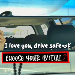 May include: Rearview mirror with the text "I love you, drive safe ♡k". Below the text is a red rectangle with the words "CHOOSE YOUR INITIAL". The image is taken from inside a car.