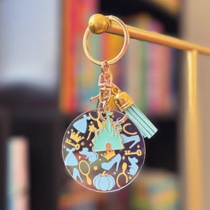 魔法のプリンセスと城をテーマにしたアクリルキーチェーン。ゴールドトーンのキーリング、ブルーのタッセル、城のチャーム付き。