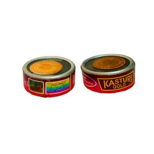 Pode incluir: Duas pequenas latas redondas, vermelhas e douradas, com o texto "KASTURI GOLD" e escrita árabe. As latas têm um centro castanho escuro e um selo dourado. Os rótulos apresentam desenhos e texto coloridos.