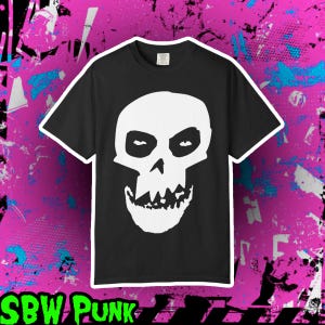 Puede incluir: Camiseta negra con un diseño de calavera blanca. La calavera tiene una expresión amenazante con dientes afilados y cuencas oscuras. La camiseta se presenta sobre un fondo rosa y azul con el texto "SBW PUNK" en verde.