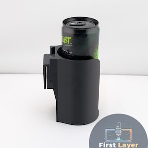 May include: Black car cup holder with a can of green energy drink. The cup holder is designed to clip onto a car's air vent. The energy drink can has the word "EAST" printed on it. A logo for "First Layer Fanatics" is in the bottom right corner.