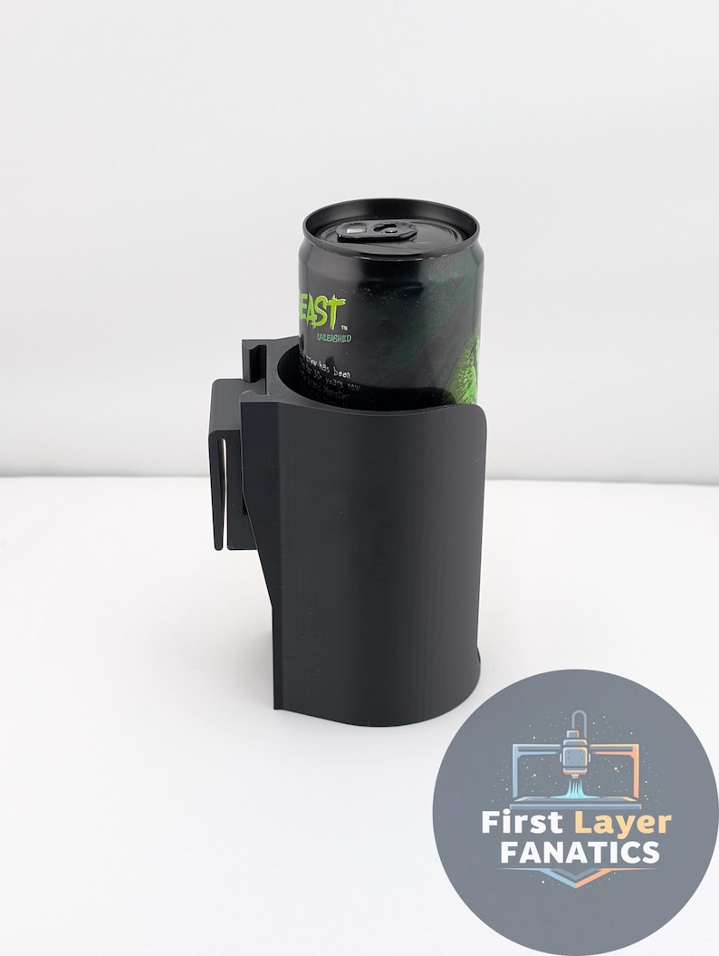 May include: Black car cup holder with a can of green energy drink. The cup holder is designed to clip onto a car's air vent. The energy drink can has the word "EAST" printed on it. A logo for "First Layer Fanatics" is in the bottom right corner.