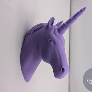 May include: A lavender unicorn head wall decoration with a detailed horn, ears, and facial features. The unicorn head is mounted on a white wall, creating a whimsical accent. The design is a fantasy-themed item for home decor.