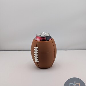 May include: A brown football-shaped can cooler with white stitching detail, holding a red and black can. The cooler is designed to keep beverages cold. The background is plain white.