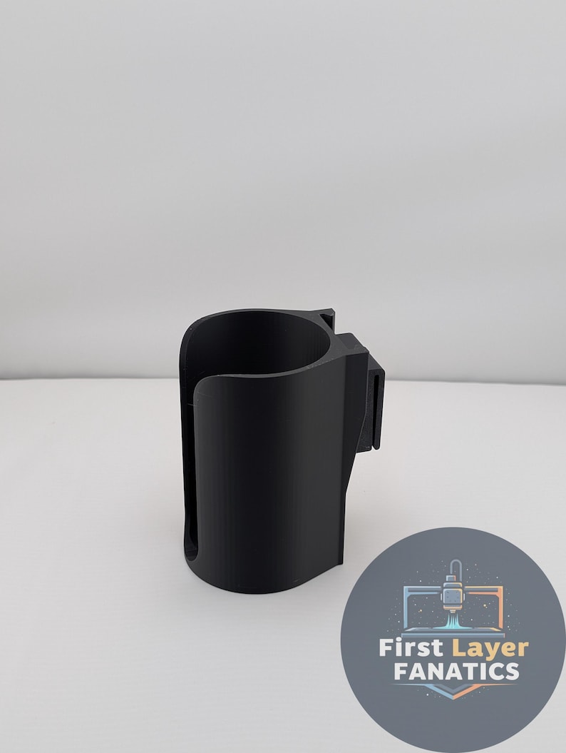 May include: A black 3D-printed cup holder with a curved design and a mounting clip. The cup holder is designed to hold a standard-sized beverage container. The image also includes a circular logo with the text "First Layer FANATICS".