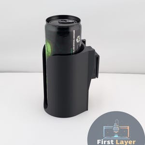 May include: A black 3D-printed cup holder with a can inside. The cup holder has a curved design and a clip for attachment. The can is black with green and white text. The logo for First Layer Fanatics is in the bottom right corner.