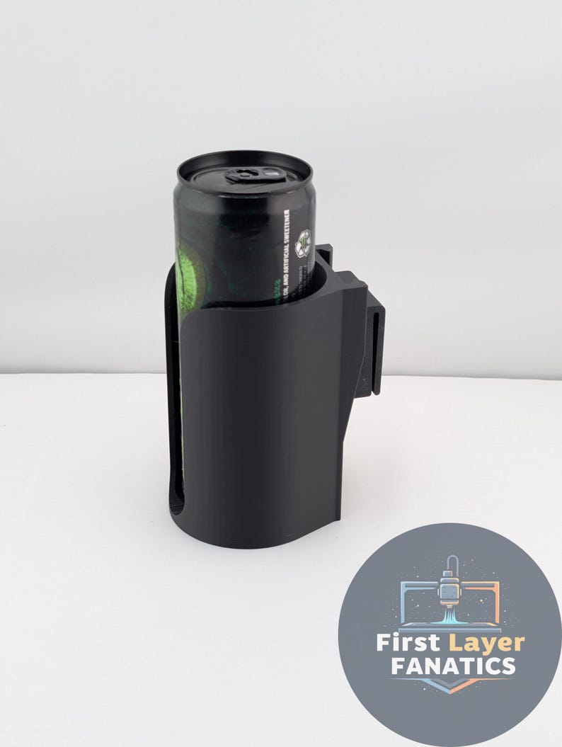 May include: A black 3D-printed cup holder with a can inside. The cup holder has a curved design and a clip for attachment. The can is black with green and white text. The logo for First Layer Fanatics is in the bottom right corner.